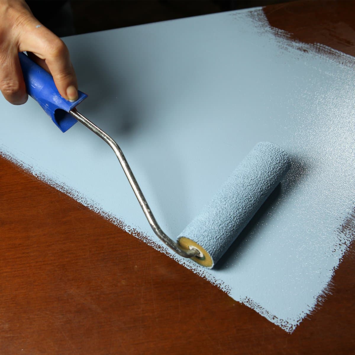 Applying Chalk It! paint to a wooden table with a roller